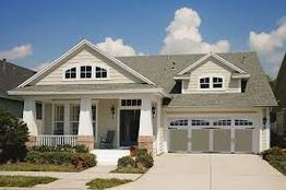 Suburban house with grey roof, garage, front porch, and manicured lawn under a blue sky.