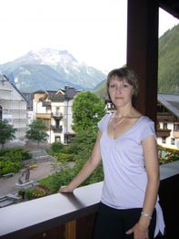 Eine Frau steht auf einem Balkon mit Bergblick im Hintergrund.