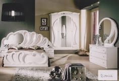 Witte slaapkamer met sierlijk bed, kast en ladekast met spiegel, op een beige vloerkleed.
