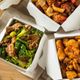 Takeout boxes filled with beef and broccoli, spicy chicken, and sweet and sour chicken on a table.