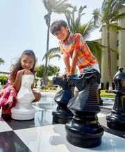Niños jugando ajedrez gigante al aire libre en un día soleado.