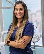 Mujer sonriente con uniforme azul en consultorio dental, con brazos cruzados.