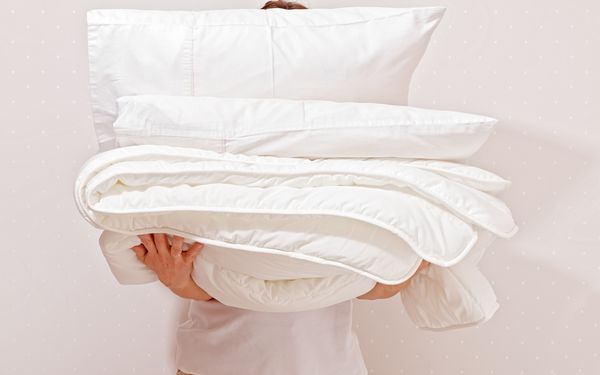 Eine Person hält einen Stapel allergikerfreundliche Bettware vor ihrem Körper.