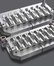 Zwei glänzende metallische Werkzeugformen auf grauem Hintergrund, symmetrisch angeordnet.