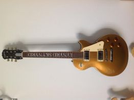 Goldene E-Gitarre, Les Paul Stil, an einer weißen Wand aufgehängt.
