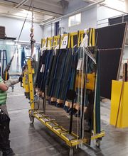 Person in Fabrik bedient Maschine, die große Glasscheiben trägt. Schutzbekleidung ist sichtbar.