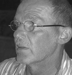 Ein Mann mit Brille und gestreiftem Hemd in Schwarz-Weiß profiliert links.