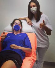 Dos personas con mascarillas, una acostada y otra de pie, mostrando pulgares arriba en señal positiva.