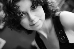 Schwarz-Weiß-Porträt einer lächelnden Person mit lockigem Haar und ärmellosem Top.