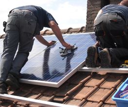 Personas instalando paneles solares en el tejado de una casa bajo un cielo despejado.