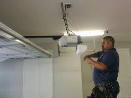 Man fixing a garage door opener, standing on a ladder, with tools in his waistband.