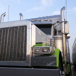 Close-up of a large semi-truck with green accents against a blue sky.