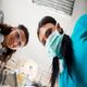 Dentist and assistant wearing masks and goggles, smiling, with dental light in background.