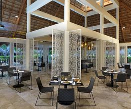 Restaurante moderno y elegante con mesas, sillas y decoración minimalista en techo de palapa.