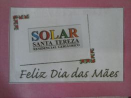 Cartão com "Solar Santa Tereza" e "Feliz Dia das Mães" em fundo rosa com detalhes florais.