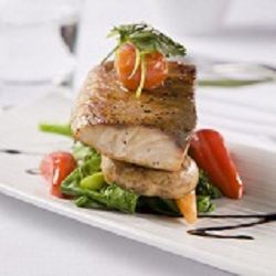 Gourmet fish dish with vegetables, garnished with tomatoes and herbs on a white plate.
