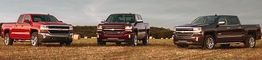 Three pickup trucks parked on a field under a cloudy sky.