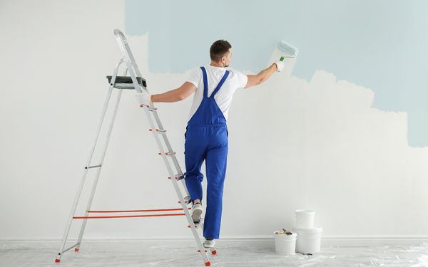 Ein Maler streicht eine Wand mit hellblauer Energiesparfarbe.