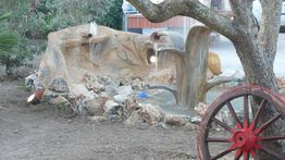 Fontana artistica di rocce con giochi d'acqua e ruota di carro in legno nel giardino.
