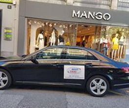 Schwarzes Auto vor einem Mango-Geschäft geparkt. Links ein Schild.