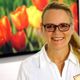 Frau mit Brille lächelt vor einem Hintergrund mit roten und gelben Tulpenbildern.