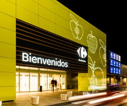 Fachada iluminada de un supermercado con el letrero "Bienvenidos" en letras brillantes.