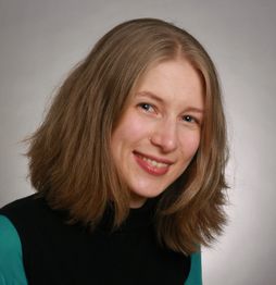 Eine Frau mit schulterlangem Haar lächelt vor neutralem Hintergrund.