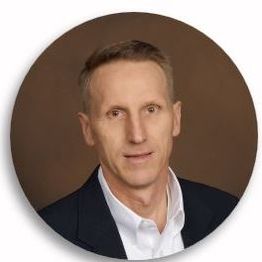 Man in a suit and white shirt against a brown background.