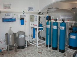 Sala de tratamiento de agua con tanques y filtros azules, etiquetado como ósmosis inversa.