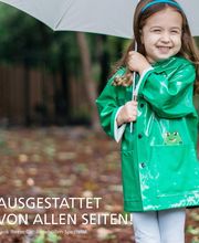 Ein Mädchen in einem grünen Regenmantel hält einen weißen Regenschirm und lächelt.