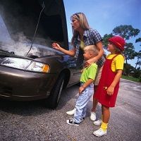 Woman and two kids standing by a car with an open hood, steam rising from the engine.