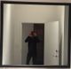 Person in dark clothing and red cap takes a mirror selfie in a room with an open door.