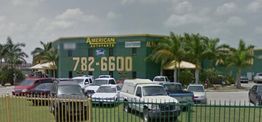 Green building with "American Auto Parts" sign, surrounded by parked cars and palm trees.