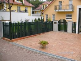 Gelbes Haus mit grünem Zaun, gepflastertem Hof und Topfblume, aufgenommen am 12.08.2015.