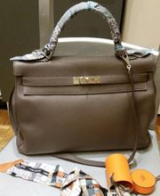 Braune Handtasche auf einem Stuhl, mit Tüchern und einem kleinen orangen Behälter daneben.