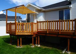Elevated wooden deck with railing attached to a house, featuring a sunshade above.