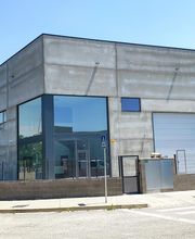 Edificio industrial moderno con fachada de vidrio y concreto, cielo despejado y furgoneta blanca.
