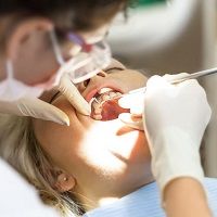 Dentist examines a patient's teeth with a dental mirror and light.