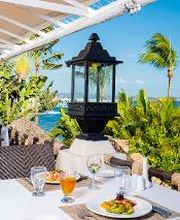 Restaurante al aire libre con vista al mar, mesas con manteles blancos y comida servida.