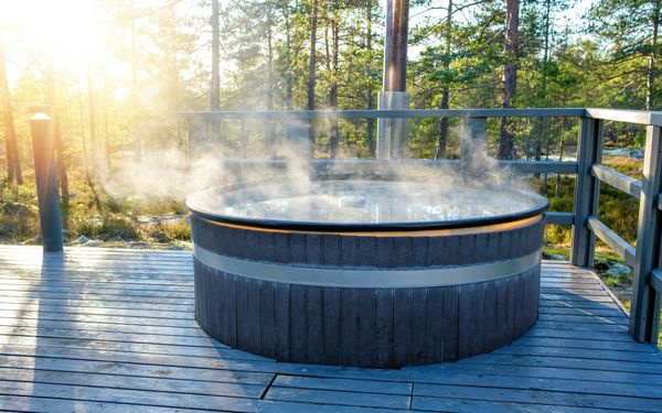 Ein Hot Tub, der mit einem Holzofen beheizt wird, steht auf einer Terrasse im Wald.