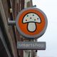 Rond bord met paddenstoel en tekst "smartshop" aan een gevel.