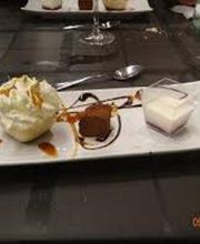 Postre en plato rectangular con mousse, trufa de chocolate, crema y cucharas sobre mesa oscura.