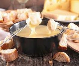 Käsefondue mit Brotstücken auf Spießen in einer schwarzen Schüssel auf Holztisch.