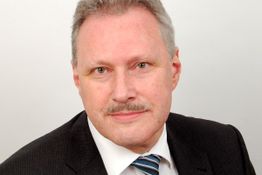 Ich weiß nicht, wer auf dem Bild ist. Ein Mann in Anzug mit Krawatte vor neutralem Hintergrund.