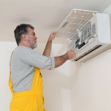 Technician in yellow overalls inspecting an air conditioner on a wall.