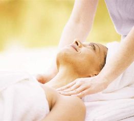 Person erhält entspannende Nackenmassage, lächelnd und in weiße Handtücher gehüllt.