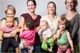 Vier Frauen halten vier Kinder auf dem Arm, alle lächeln in die Kamera.
