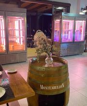 Restaurante con vitrinas iluminadas, mesa con platos y cristalería, barril decorativo.