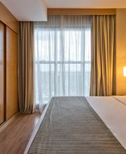 Quarto de hotel com cama de casal, TV, janela com cortinas e iluminação suave.