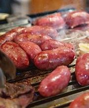 Churrasco com linguiças e bifes grelhados em uma churrasqueira.